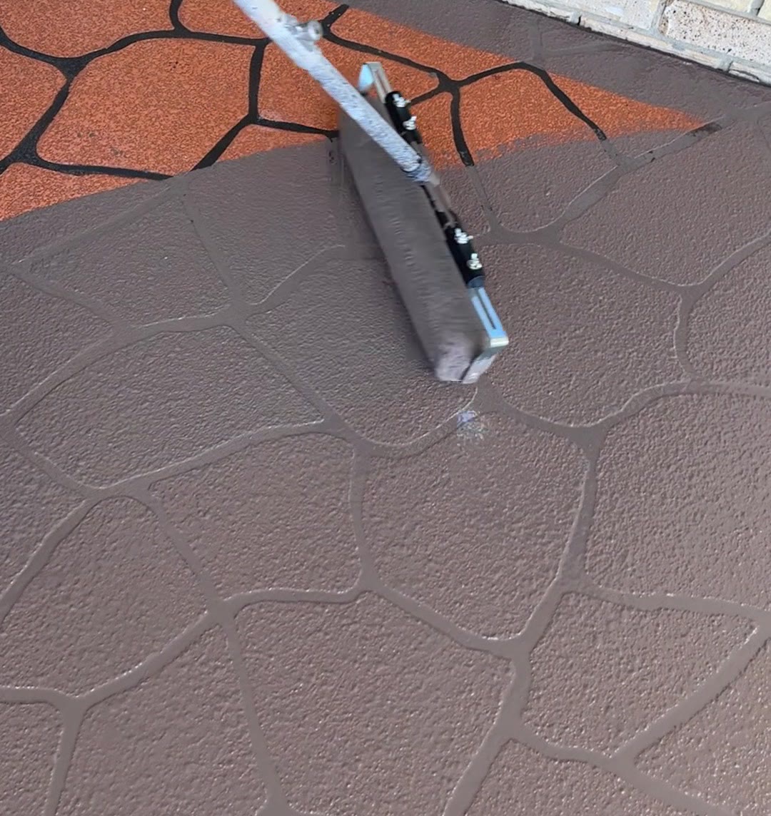 Rolling coloured sealer across a stencilled crazy-pave driveway mid-application